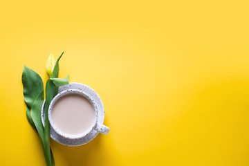Cup of coffe with a yellow tulips over yellow background