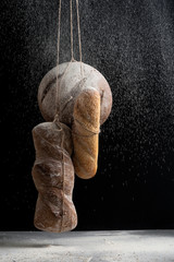 Three kinds of fresh bread in a fog of flour on a black background.