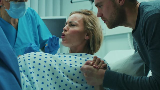 In the Hospital, Close-up on a Woman in Labor Pushing Hard to Give Birth, Obstetricians Assisting, Spouse Holds Her Hand. Shot on RED EPIC-W 8K Helium Cinema Camera.