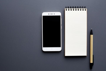 blank notepad with smartphone and pen over gray background