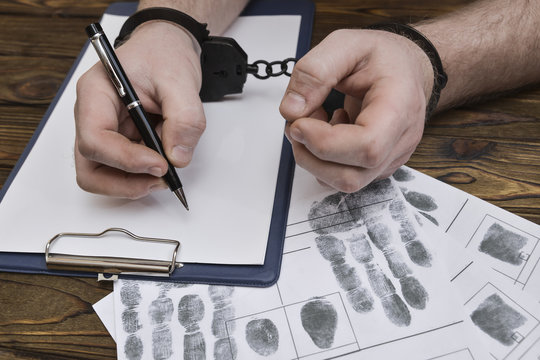 Men's hands with handcuffs fill the police record, confession. on top of the police investigative detective. Arrest, bail, criminal, prison. fingerprints, criminalist. the attacker. close-up