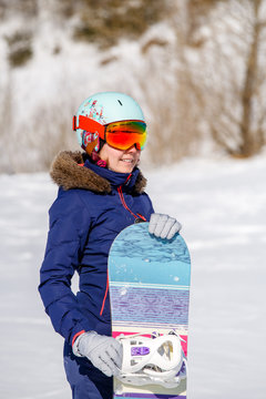 Portrait of smiling sportswoman in helmet with snowboard in winter day