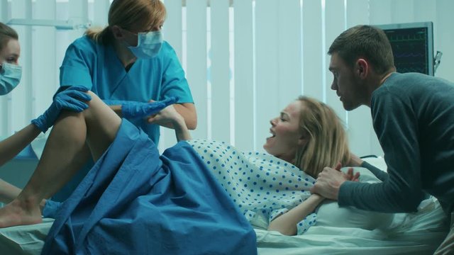 In the Hospital Woman in Labor Pushes to Give Birth, Obstetricians Assisting, Spouse Supports Her by Holding Hand. Shot on RED EPIC-W 8K Helium Cinema Camera.