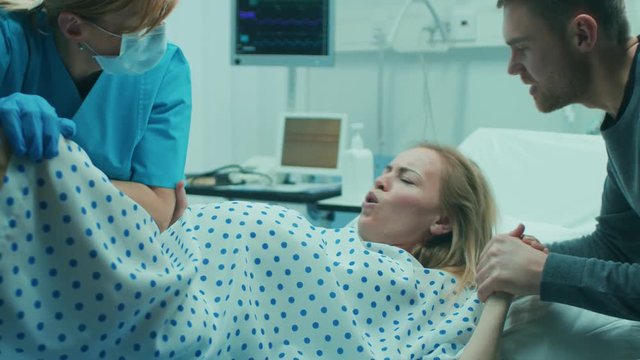 In the Hospital Woman in Labor Pushes to Give Birth, Obstetricians Assisting, Husband Holds Her Hand for Support. Shot on RED EPIC-W 8K Helium Cinema Camera.