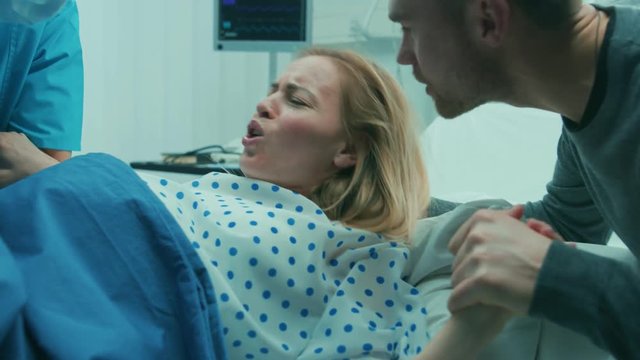 In the Hospital Close-up on Woman in Labor Pushes to Give Birth, Obstetricians Assisting, Husband Holds Her Hand. Shot on RED EPIC-W 8K Helium Cinema Camera.