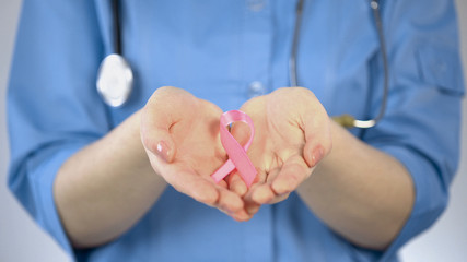 Pink ribbon lying in palms of female doctor, breast cancer awareness campaign