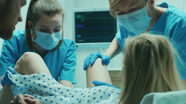 In the Hospital Woman Giving Birth, Husband Holds Her Hand in Support, Obstetricians Assisting. Modern Delivery Ward with Professional Midwives. Shot on RED EPIC-W 8K Helium Cinema Camera.