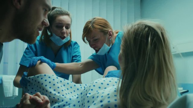 Emergency In the Hospital: Woman Giving Birth, Husband Holds Her Hand in Support, Obstetricians Assisting. Modern Delivery Ward with Professional Midwives. Shot on RED EPIC-W 8K Helium Cinema Camera.