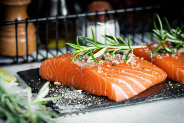 Two pieces of raw salmon fillet with fresh herb rosemary, spices and olive oil on black slate plate