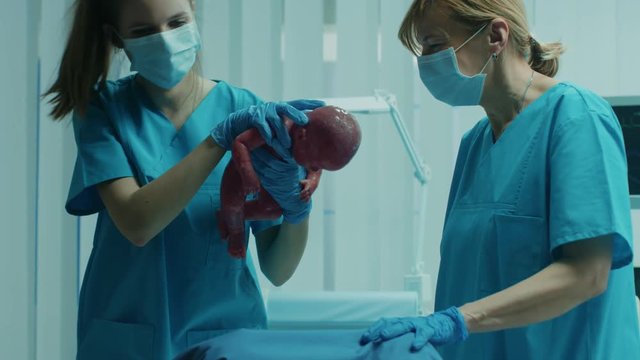 In the Hospital Woman in Labor Pushes and Gives Birth, Baby Comes out, Obstetricians Assist Delivery, Husband Supports His Wife. Side View Footage.  Shot on RED EPIC-W 8K Helium Cinema Camera.