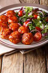 Tasty glazed meatballs with fresh vegetable salad close-up on a plate on a table. vertical