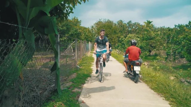 A group of young friends bicycle through a rural area covered with lush trees in Vietnam while on vacation