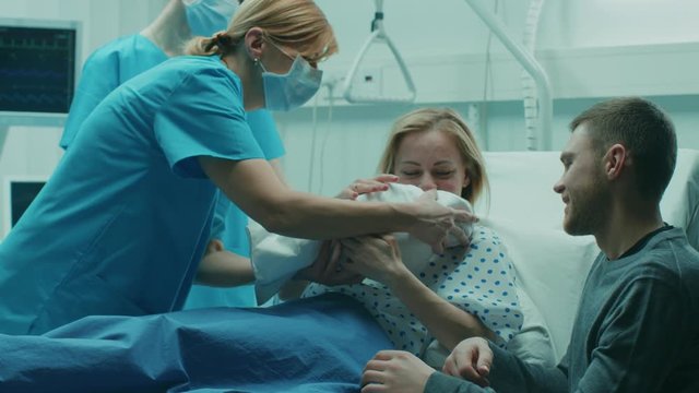 In the Hospital Midwife Gives Newborn Baby to a Mother to Hold, Supportive Father Lovingly Hugs Baby and Wife. Happy Family in the Modern Delivery Ward. Shot on RED EPIC-W 8K Helium Cinema Camera.
