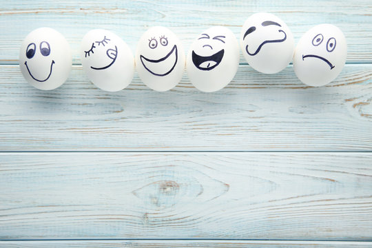 Eggs with funny faces on wooden table