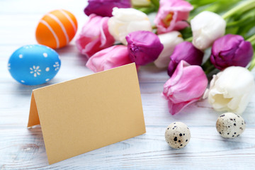 Blank card with painted eggs and tulips on wooden table