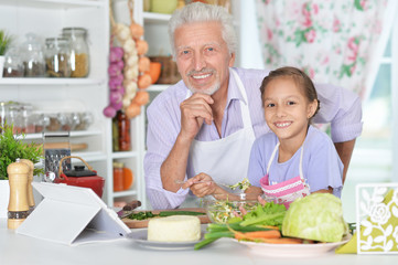 Senior man with granddaughter preparing dinner in kitchen