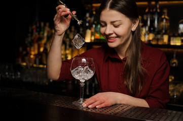 Smiling female barman putting ice cubes into a glass making an Aperol syringe cocktail