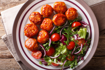 Tasty glazed meatballs with fresh vegetable salad close-up on a plate. horizontal top view