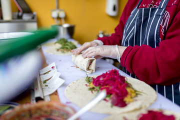 Fresh and delicious chicken shish kebab being prepared hygienically in a burritos or fajitas wrap and covered with salad including red lettuce, grated carrots, rocket leaves