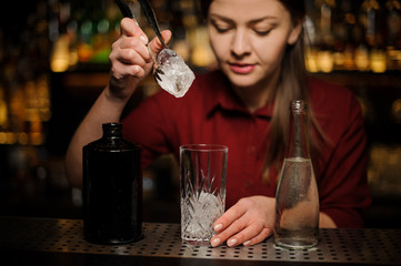 Young female bartender putting an ice cube into a glass