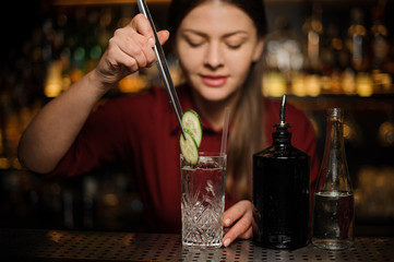 Female bartender making a fresh cocktail with gin and cucumber