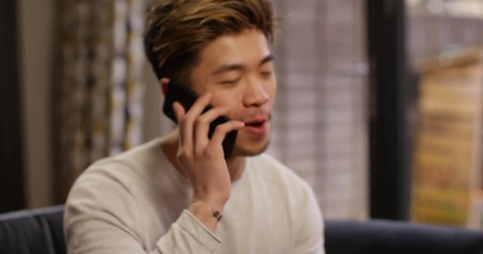 4K Camera pulls back from close up of cheerful Asian man talking on phone. Slow motion.