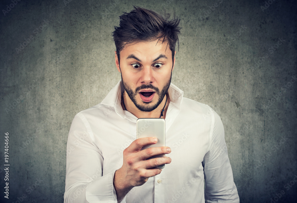 Wall mural surprised young man watching smartphone