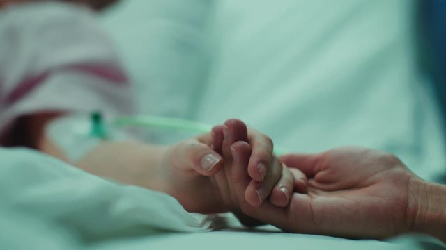 Recovering Little Child Lying in the Hospital Bed Sleeping, Mother Holds Her Hand Comforting. Focus on the Hands. Emotional Family Moment.  Shot on RED EPIC-W 8K Helium Cinema Camera.