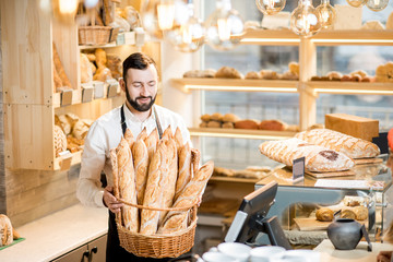 Fototapeta na wymiar Handsome bread seller with basket full of baguettes in the beautiful store with bakery products