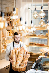 Handsome bread seller with basket full of baguettes in the beautiful store with bakery products