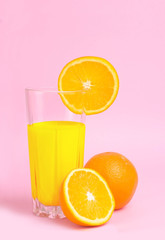 A glass with orange juice with the cut oranges on a pink background. Juicy color scale, pin up, pop up styles. Food for breakfast, a healthy drink with vitamins and miniroalami. A sunny drink.