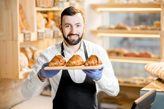 Portrait of a handsome seller in uniform standing with delicious croissants in the store with bakery products