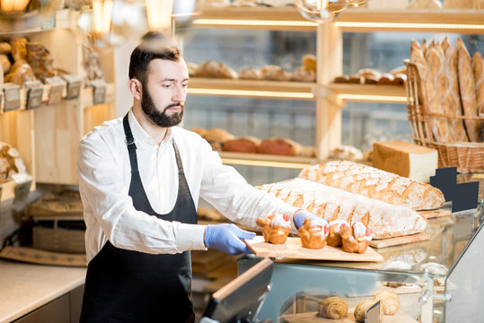 Bread seller putting maffins on the showcase standing in the beautiful store with bakery products