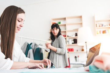 Fototapeta premium Young women dressmaster create new concept clothing with contemporary laptop in sewing showroom. Small business. Seamstress working with cloth in workshop