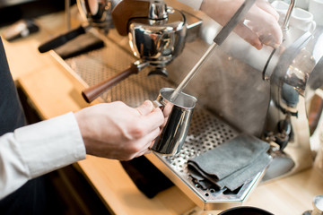 Barista whipping a milk for capucciono with professional coffee machine in the cafe
