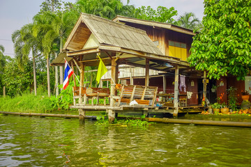 Fototapeta na wymiar Outdoor view of floating poor house with two falgs at the enter of the building on the Chao Phraya river. Thailand, Bangkok