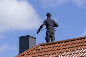 Chimney sweep cleaning a chimney standing on the house roof, lowering equipment down the flue