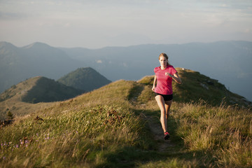 Fototapeta premium Woman runs on a top of the mountains with mountain range in background
