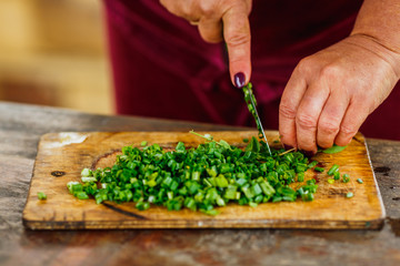 female chef cuts fresh green onion for salad