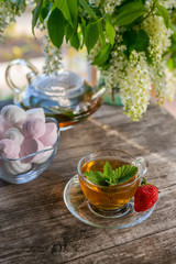 Delicious green mint strawberry tea in a transparent glass teapot and Cup in the summer, on a rustic wooden table with strawberries and marshmallows.