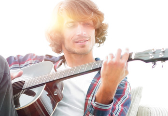 Handsome man playing on the guitar on the couch at home