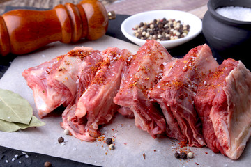 Raw fresh meat, uncooked lamb or beef ribs with pepper, garlic, salt, bay leaves and spices on dark stone background, Ready for cooking. copy space.