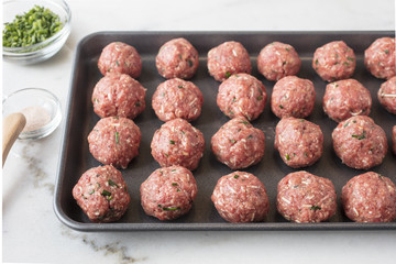 Raw meat balls prepared and ready to be baked on a sheet pan with seasonings on the side