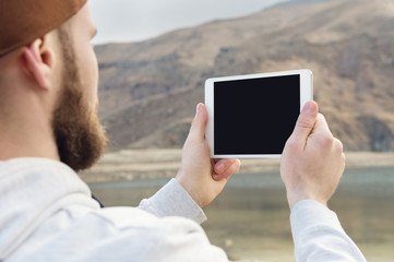 Hipster person holding in hands digital tablet with empty blank screen, man photograph on computer on background nature outdoor landscape mock up technology blur male hands tourist using gadget