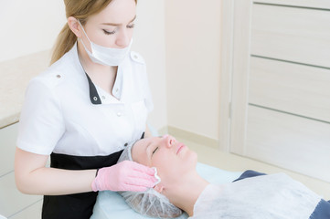 Cleaning procedure in the office of cosmetology. Cosmetologist in pink gloves are removed from the face of a young girl with a sponge cleansing the mask