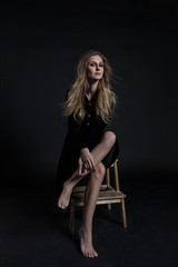 Fototapeta na wymiar Full length model in black dress posing sitting on dark background