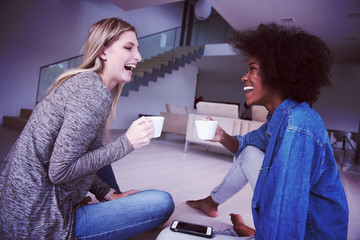 young multiethnic women sit on the floor and drinking coffee