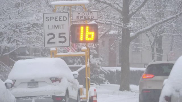 Cars travel past a speed limit warning sign on a snowy residential street. Pittsburgh suburbs. With audio.  	