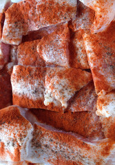 Many raw sliced fresh fish fillets pink pieces well sprinkled with red pepper, are ready for baking vertical top view closeup