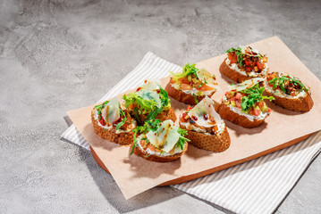 Italian bruschetta with salmon, tomatoes, cheese and basil pesto on a grey concrete or stone background.